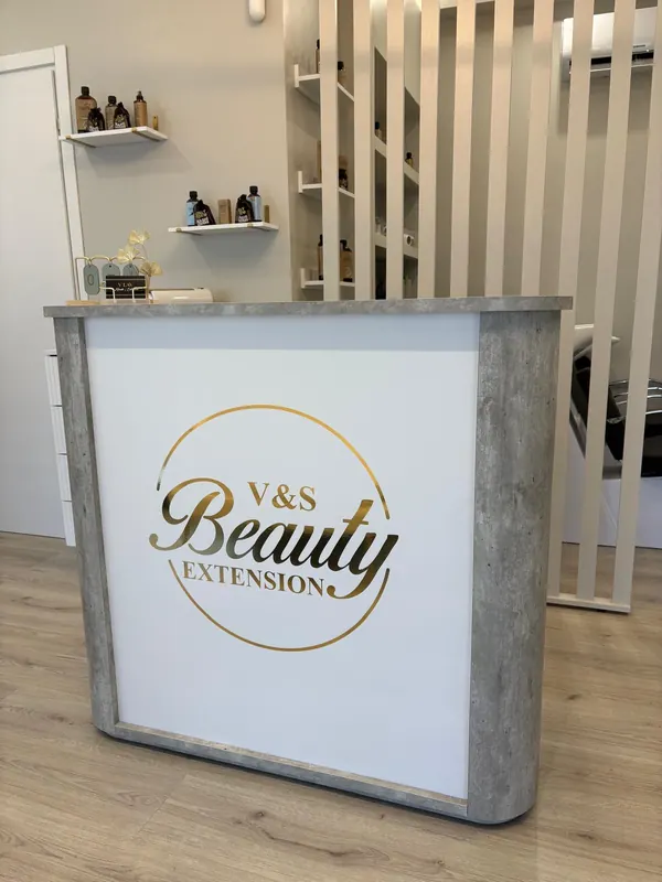 Il banco della reception in cemento grigio con il logo V&S Beauty Extension in oro, mensole con i prodotti e listelli in legno chiaro