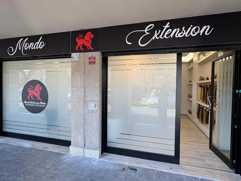 La vetrina del salone con l'insegna Mondo Extension, il leone rosso e la porta aperta sulla parete delle ciocche